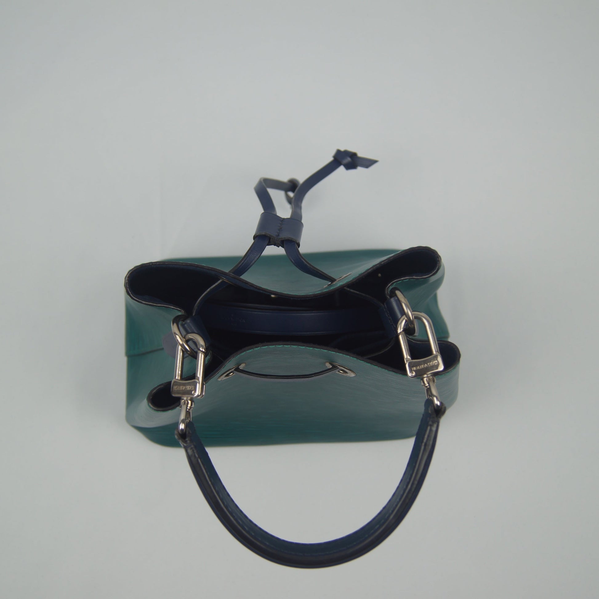 Green leather handbag with a blue handle on a light gray background