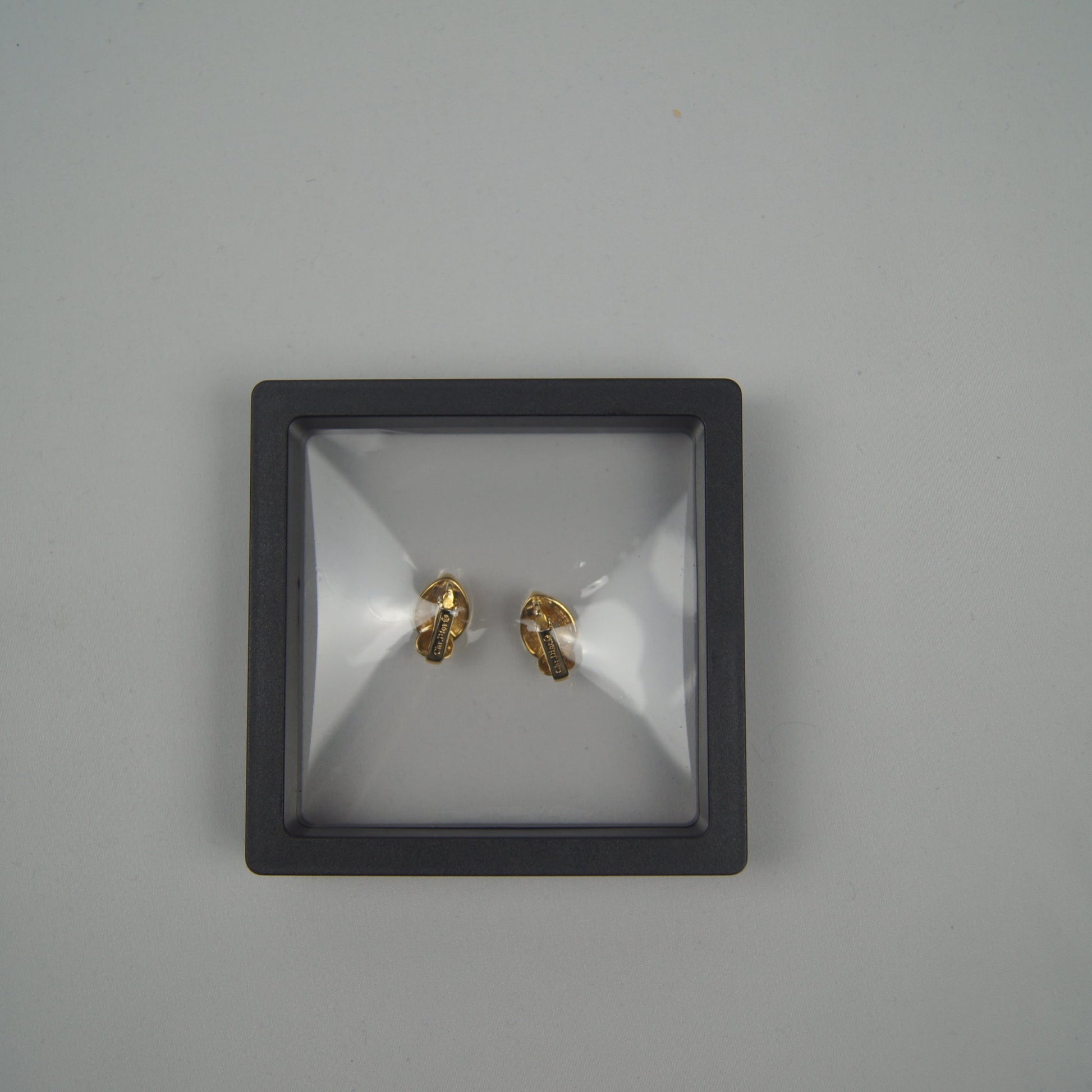 Pair of gold earrings in a black display box on a gray background