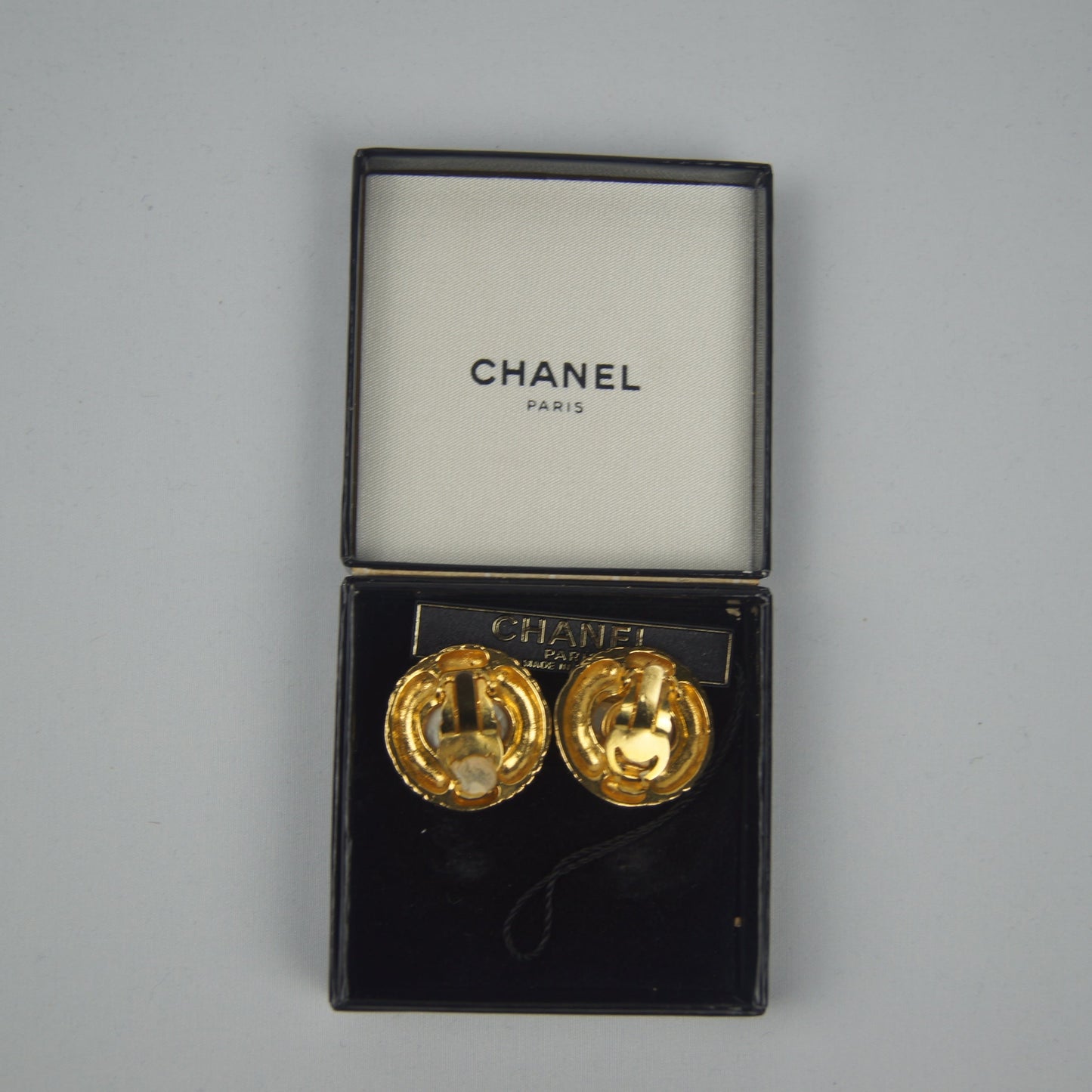 Gold earrings in a Chanel box on a gray background