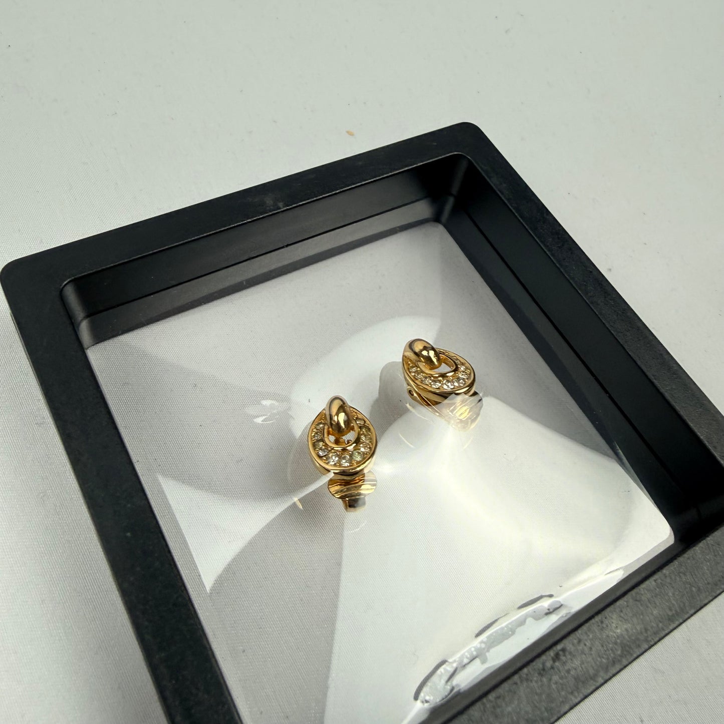 Gold earrings in a black display box on a light gray background